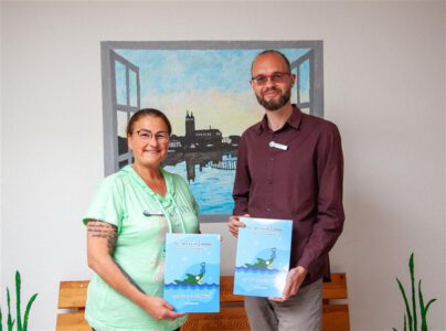 Humanas-Geschäftsführer Fabian Biastoch und Aileen Wiesner, Pflegedienstleiterin des Wohnparks in der Ulnerstraße, freuen sich über mehrere Exemplare des Kinderbuches, die nun den Humanas-Bewohnerinnen und -Bewohnern in der Ulnerstraße zum Lesen zur Verfügung stehen.